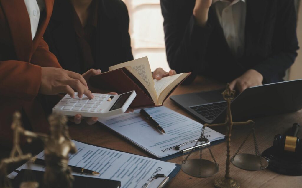 Professionals working on legal documents with a calculator, book, and laptop.